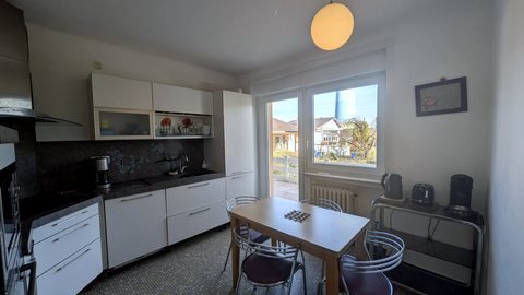 Cuisine équipée indépendante de la maison : plan de travail, four, plaques et coin repas, ouverte sur la terrasse